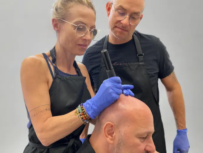 Technicienne réalisant une tricopigmentation capillaire avec gants bleus et dermographe professionnel